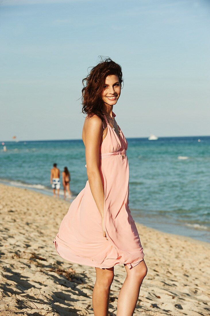 A young woman on a beach wearing a pink summer dress