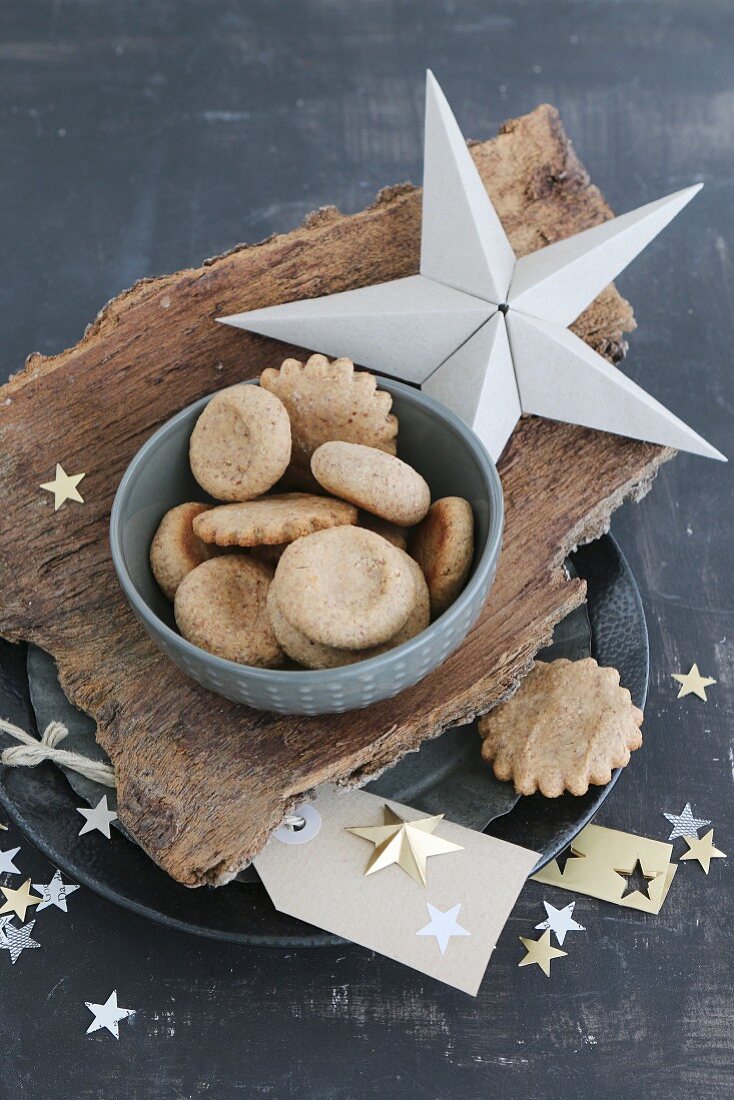 Weihnachtsplätzchen in Schale auf Baumrinde und selbstgebastelte Weihnachtssterne aus Papier und Goldfolie