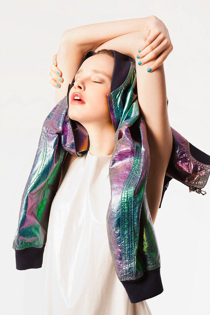 A young woman wearing a light top with a shimmering leather jacket over her head