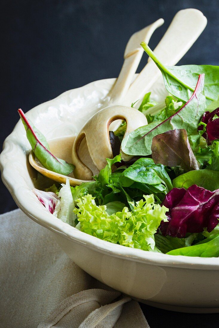 Verschiedene Blattsalate in antiker Schüssel mit Salatbesteck
