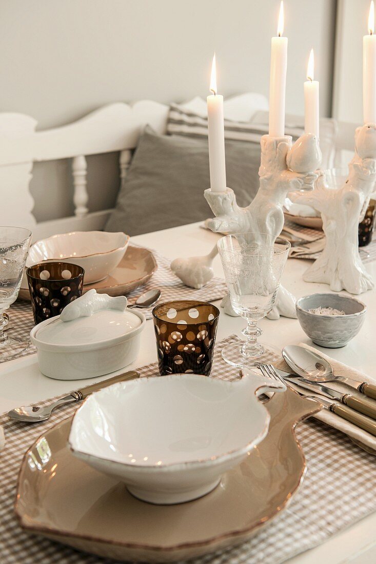 Place setting with elegant, leaf-shaped china bowl and lit candle in china candlestick on dining table