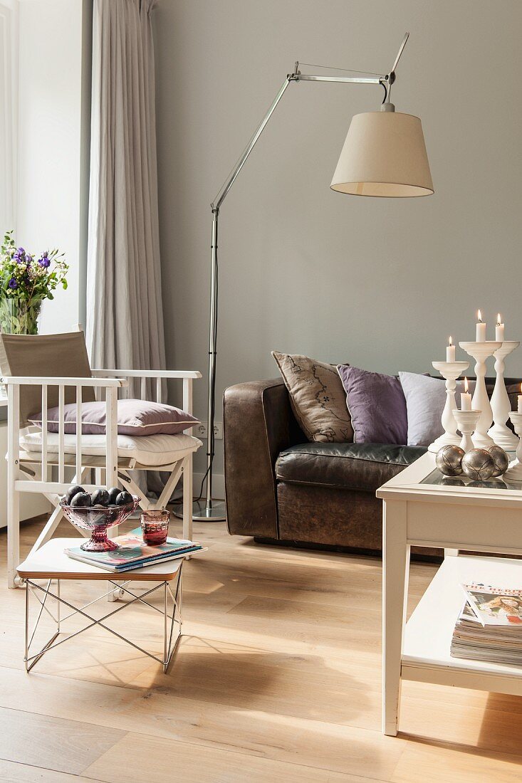 Low side table and standard lamp between armchair and leather sofa against pale grey wall