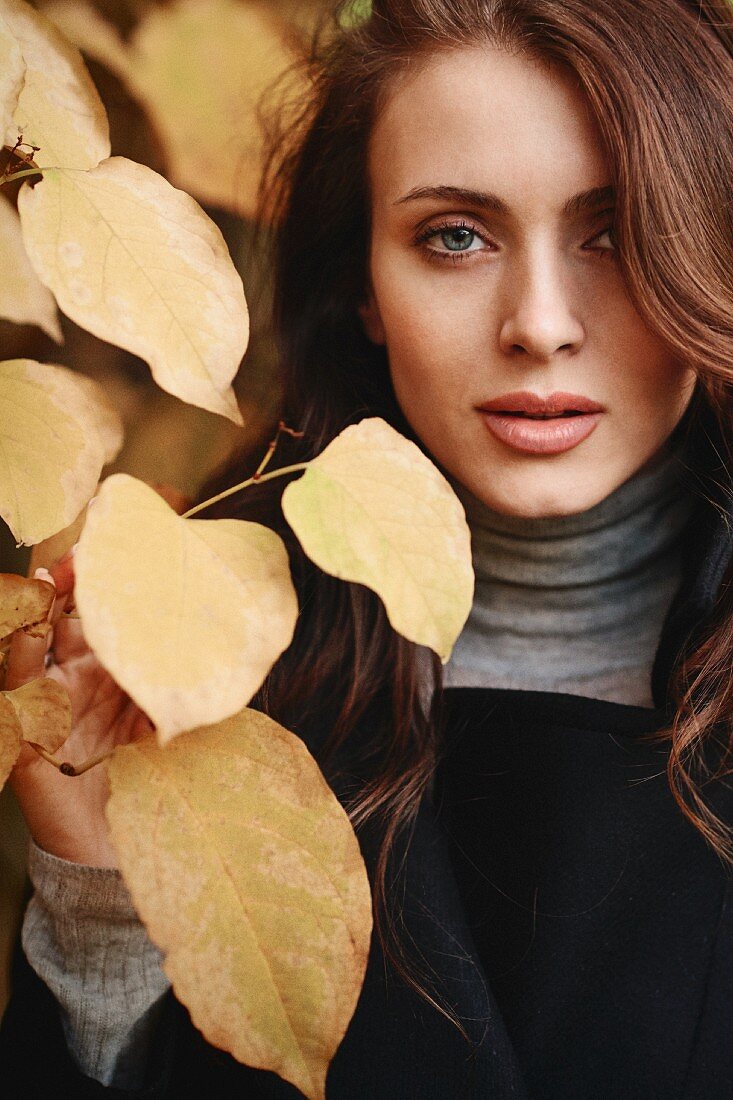 A young woman wearing a turtleneck jumper and a black jacket with autumnal leaves