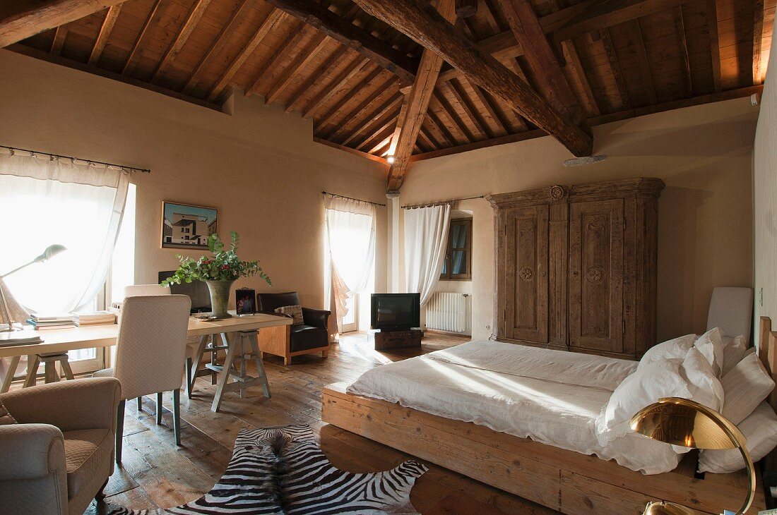 Simple double bed and desk and chair below window in attic bedroom