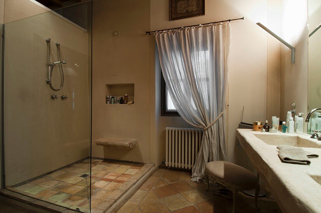 Shower with glass partition opposite masonry washstand in rustic bathroom