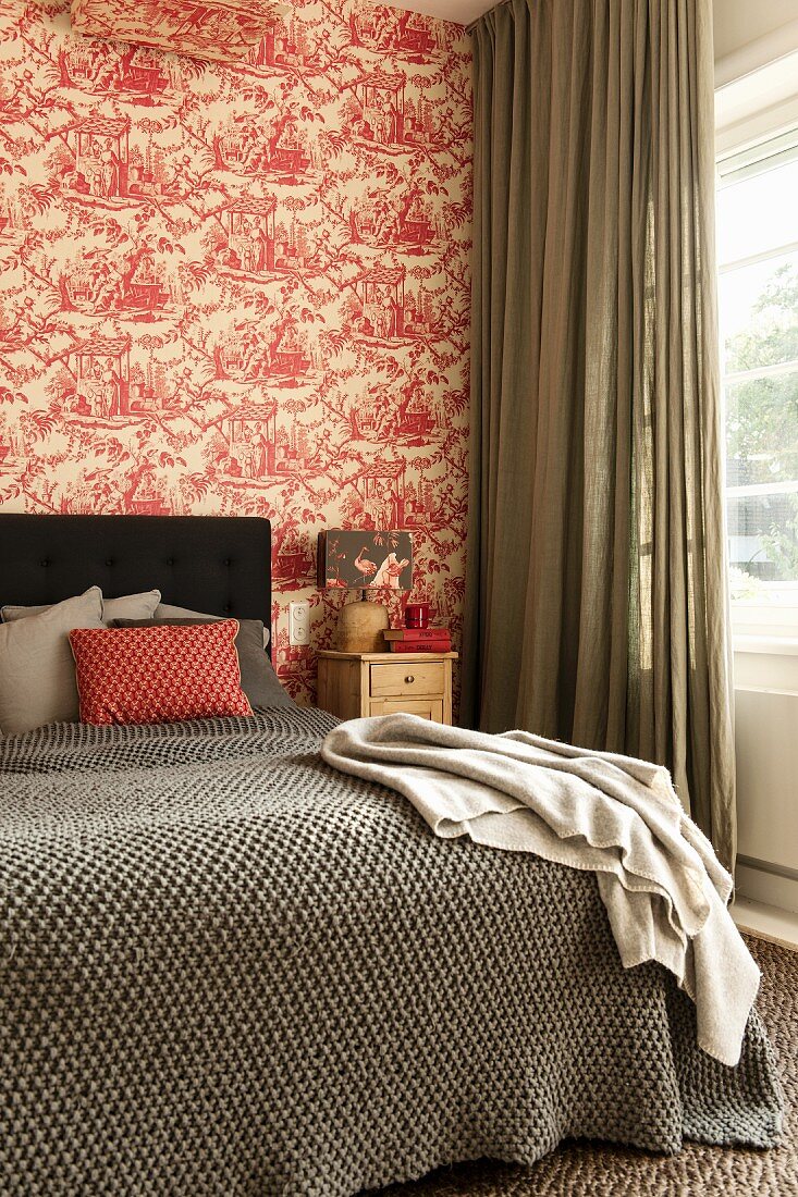 Tagesdecke auf Doppelbett mit Kopfteil vor tapezierter Wand mit rot-weißem Toile de Jouy Muster
