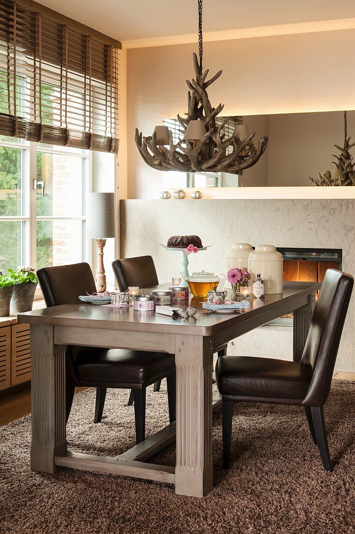 Leather chairs around set table below antler chandelier in corner of dining room