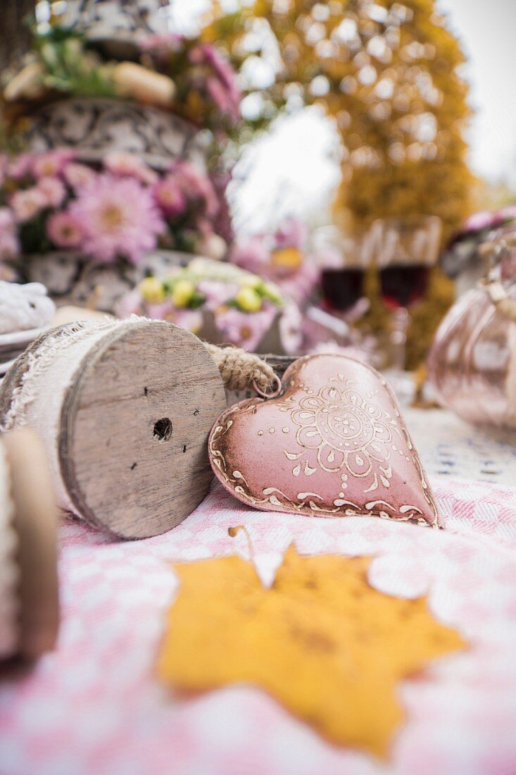 Metal heart and reel of decorative ribbon on autumnal table