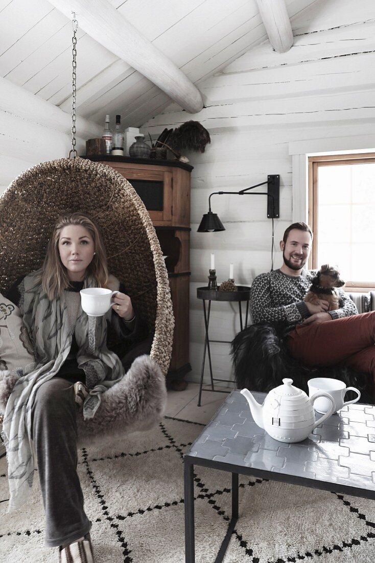 Ein junges Paar mit Hund im winterlichen Wohnzimmer einer Blockhütte