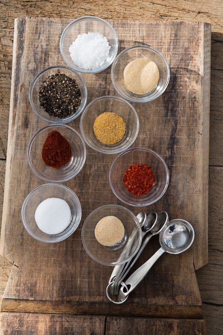 Bowls of various grill spices on a wooden board