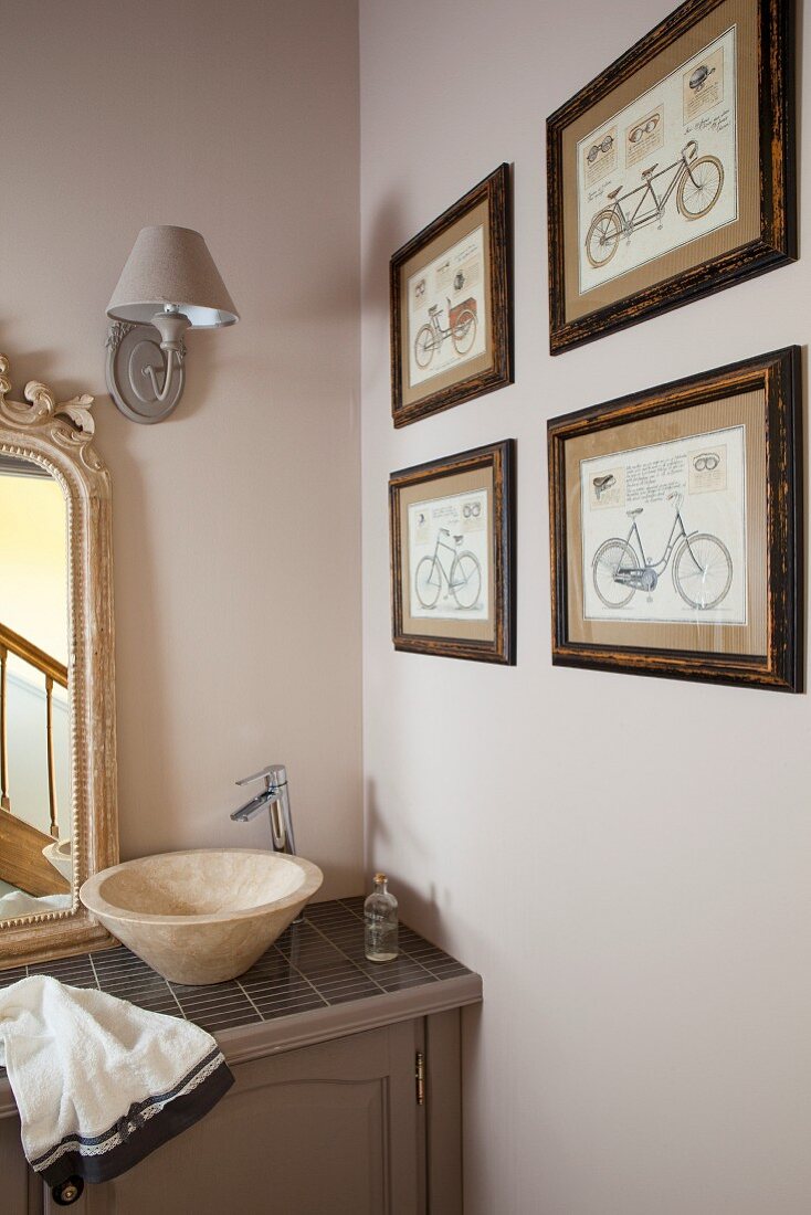 Washstand with countertop basin and modern tap in corner of bathroom next to collection of bicycle pictures on beige wall