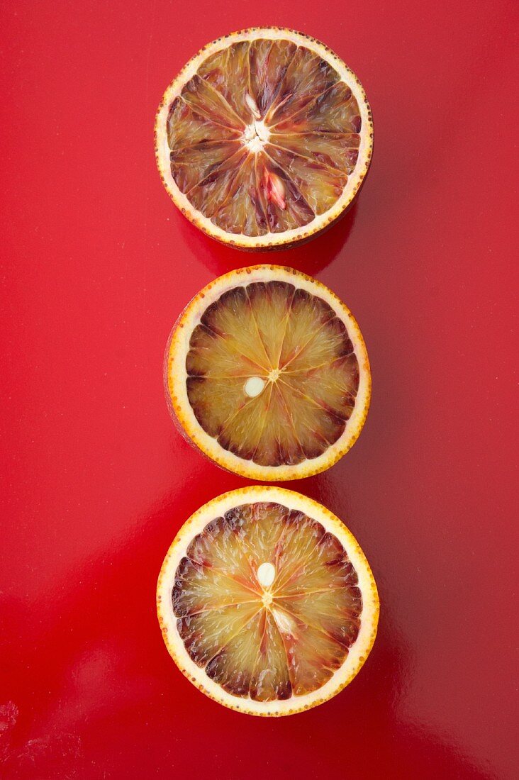 Three blood orange halves on a red surface