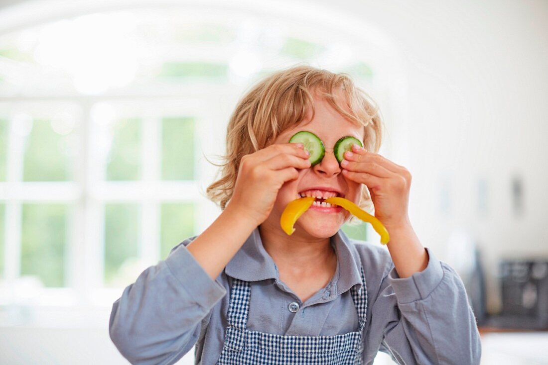 A boy playing with vegetables in a kitchen