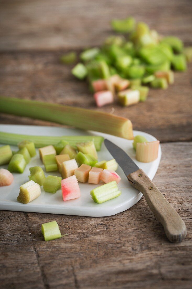 Peeled and chopped rhubarb on a ceramic board with a kitchen knife