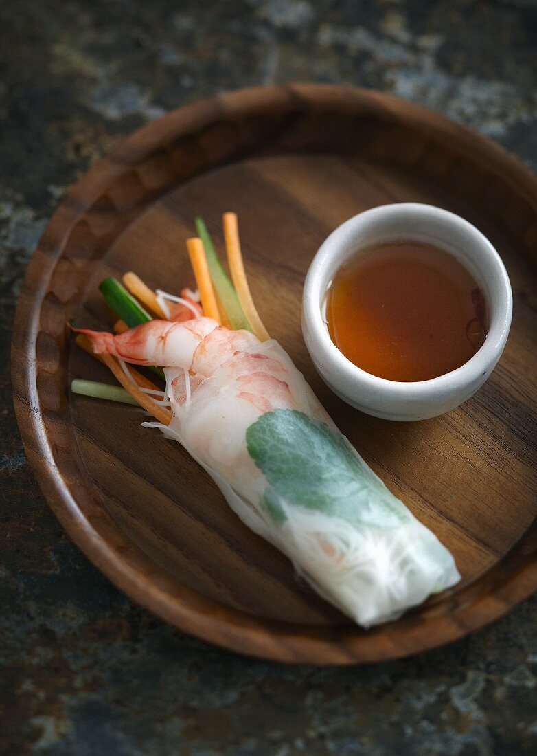 A spring roll with a prawn and vegetables filling served with soy sauce