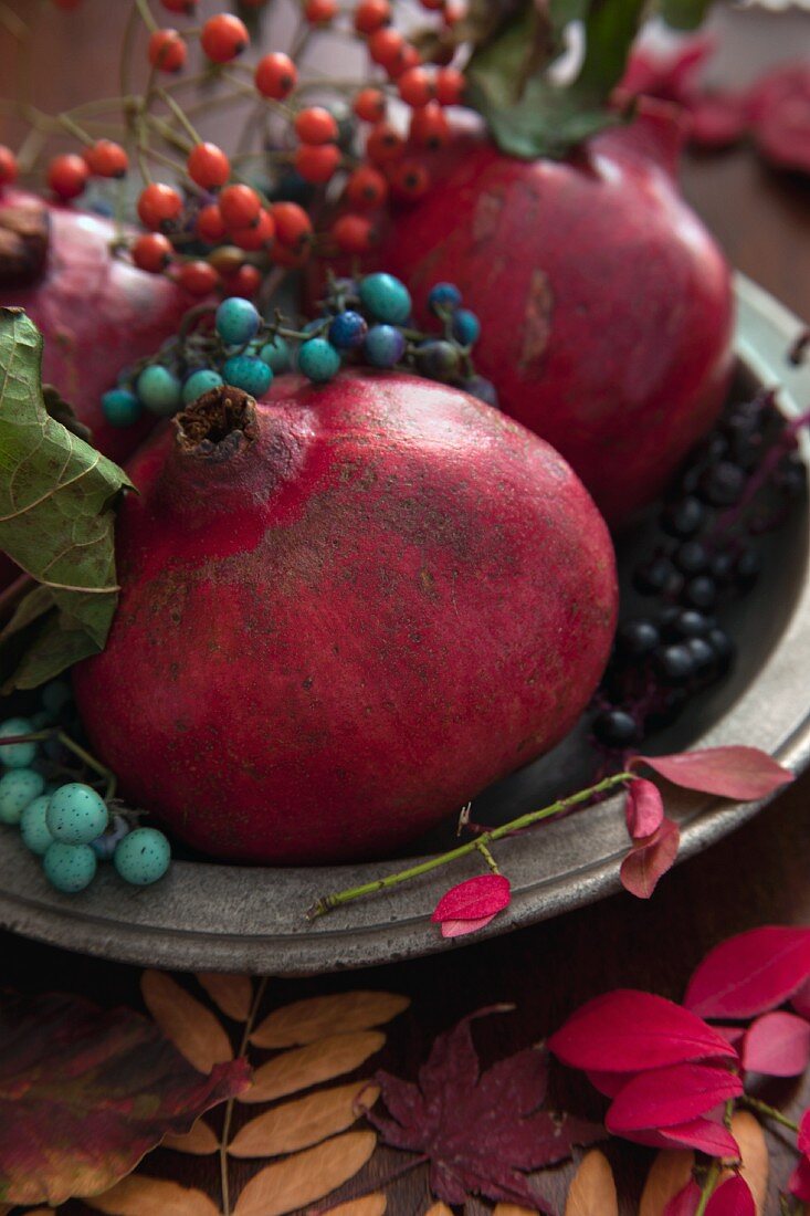 Pomegranates with autumnal sprigs of berries on a pewter plate