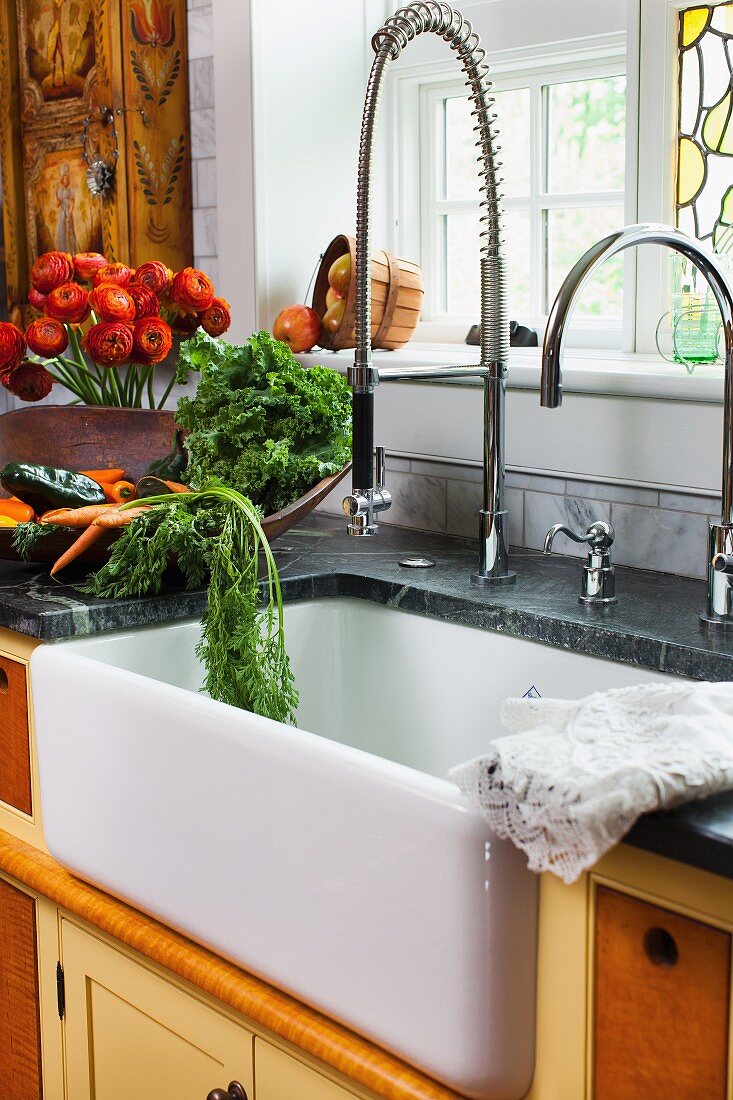 Fresh vegetables and flowers next to a sink with a modern tap in a farmhouse kitchen