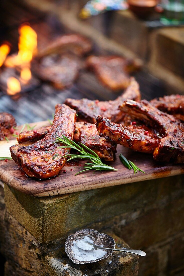 Grilled lamb chops on a wooden board next to a barbecue