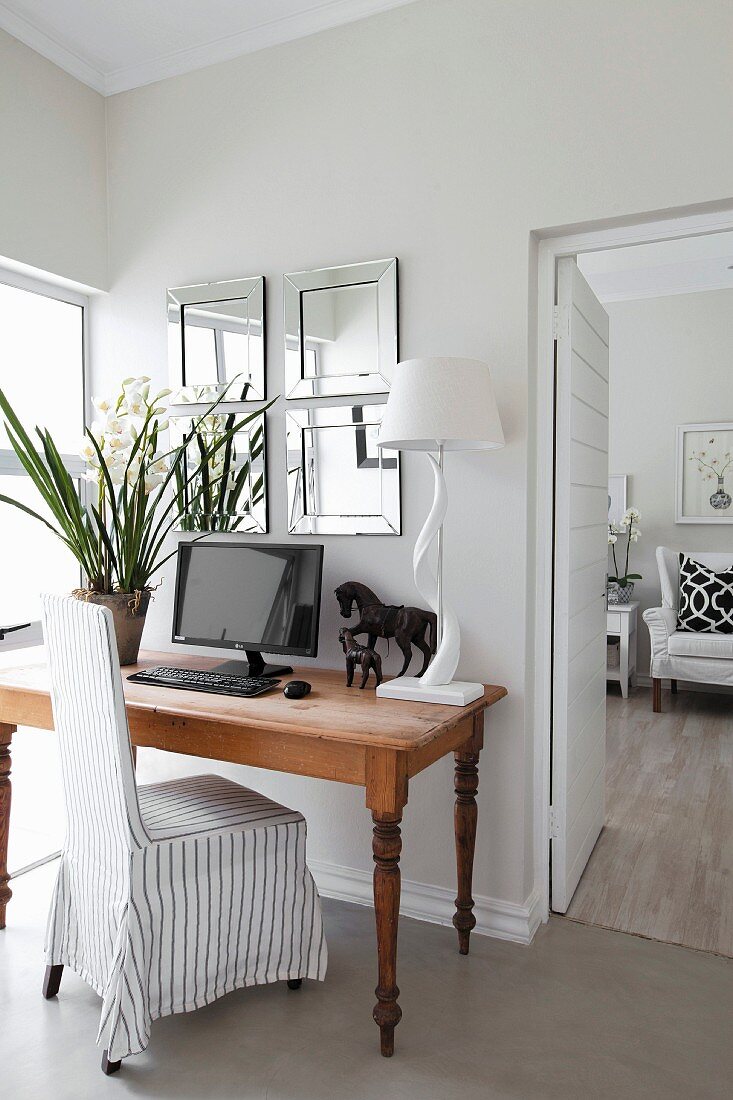 Flowers, monitor, horse ornament and table lamp on table with loose-covered chair