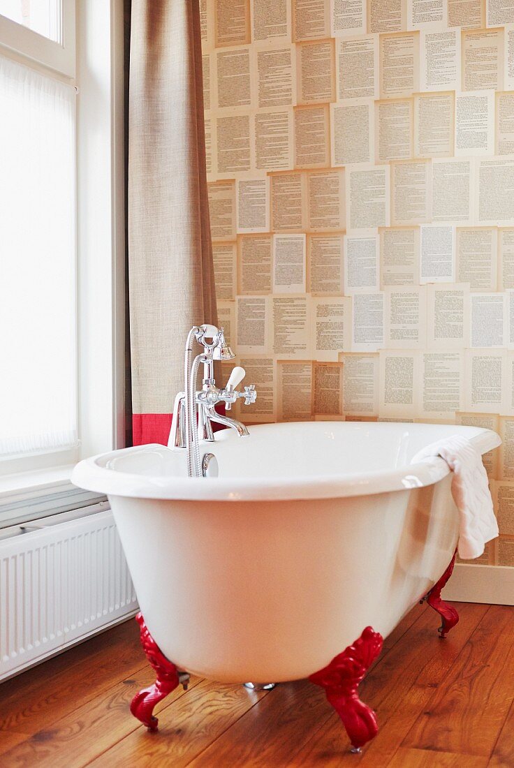 Vintage-style free-standing bathtub with red claw feet against patterned wallpaper