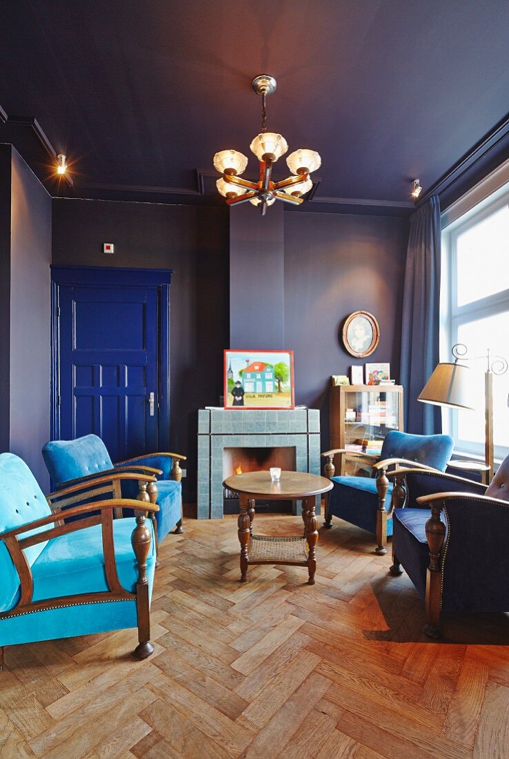 Blue salon with herringbone parquet floor, armchairs in various shades of blue and open fireplace in background