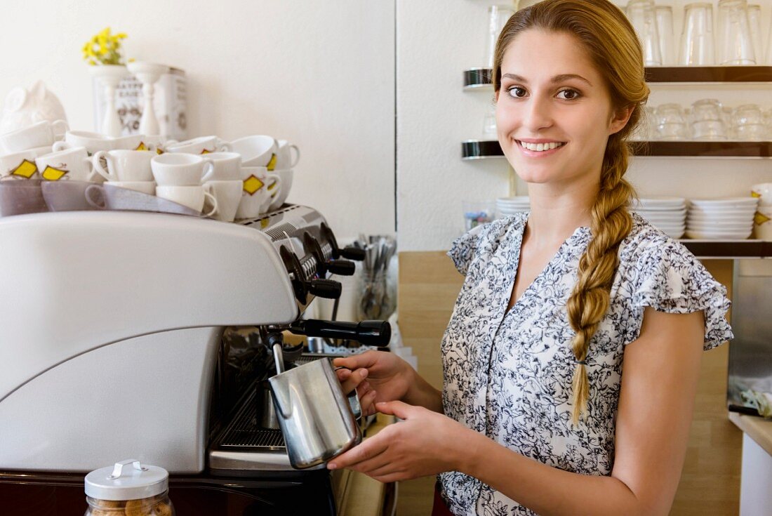 Junge Frau beim Aufschäumen von Milch an Kaffeeautomat