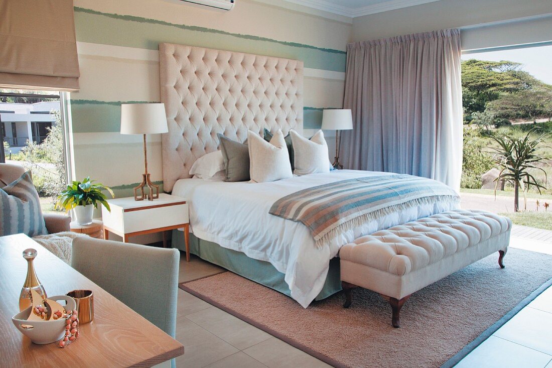 Elegant bed with button-tufted headboard and ottoman in front of open sliding door