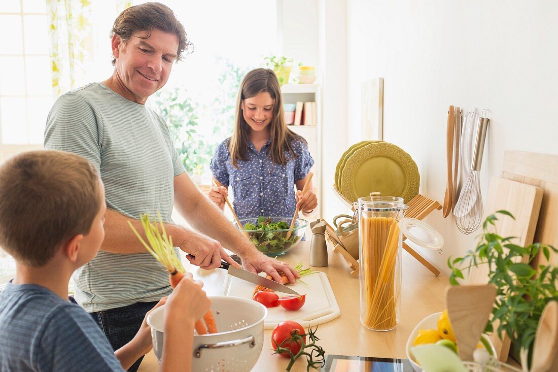 A father with his son and daughter preparing food in a kitchen