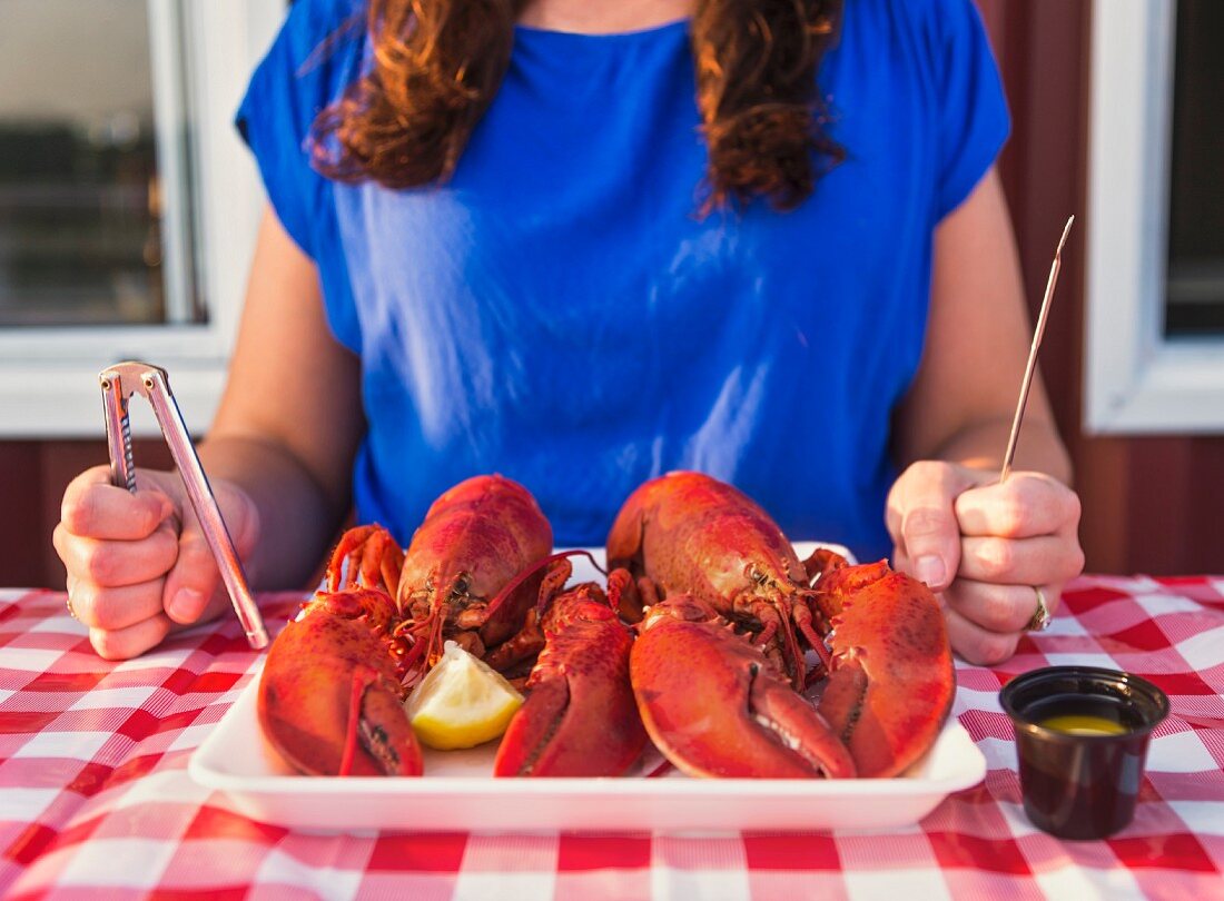 A woman holding lobster cutlery sitting in front of a platter of cooked lobster