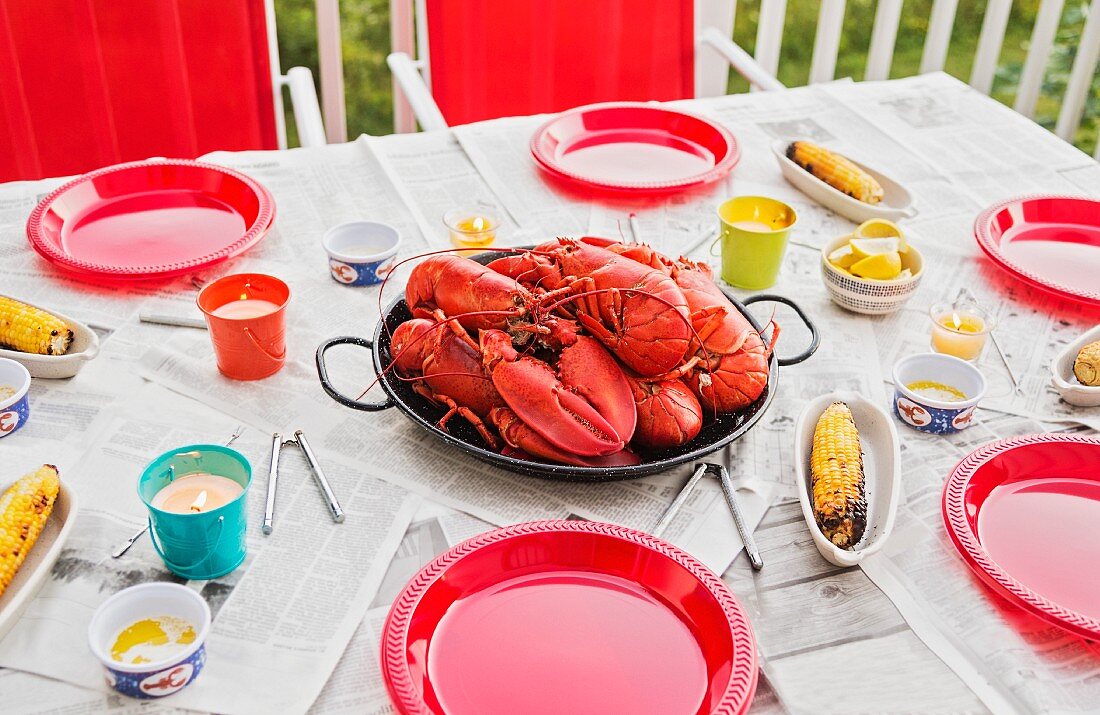 A table laid outside with lobster and corn on the cob
