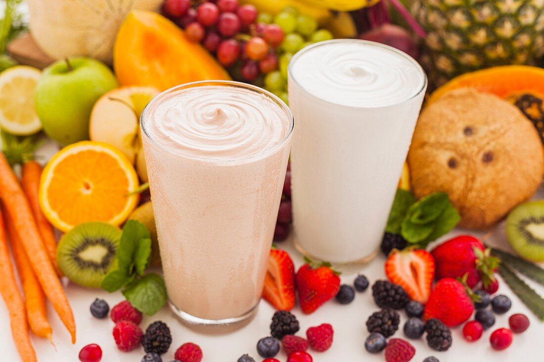 Two smoothies surrounded by fruit and vegetables