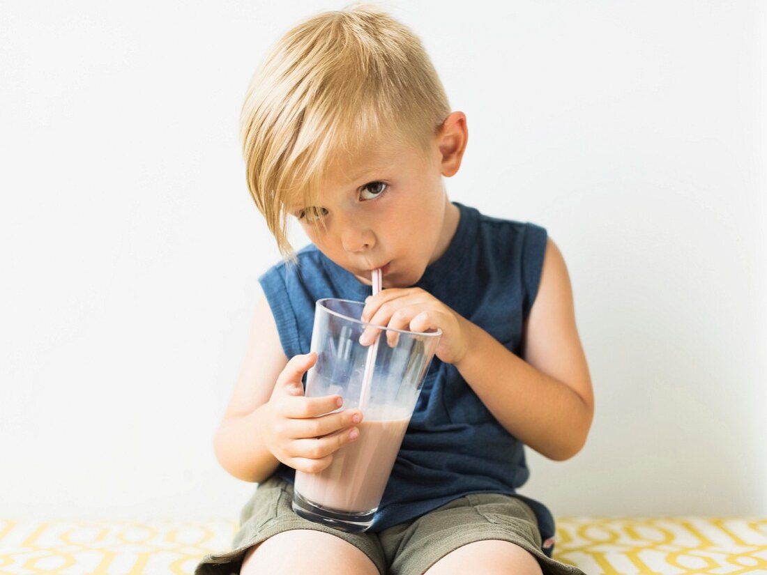 A little boy drinking a milkshake from a glass with a straw