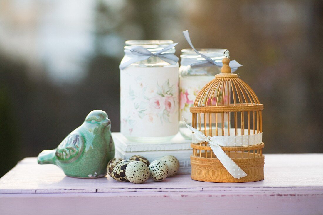 Romantic arrangement of quails' eggs, bird ornament, miniature bird cage and decorated screw-top jars