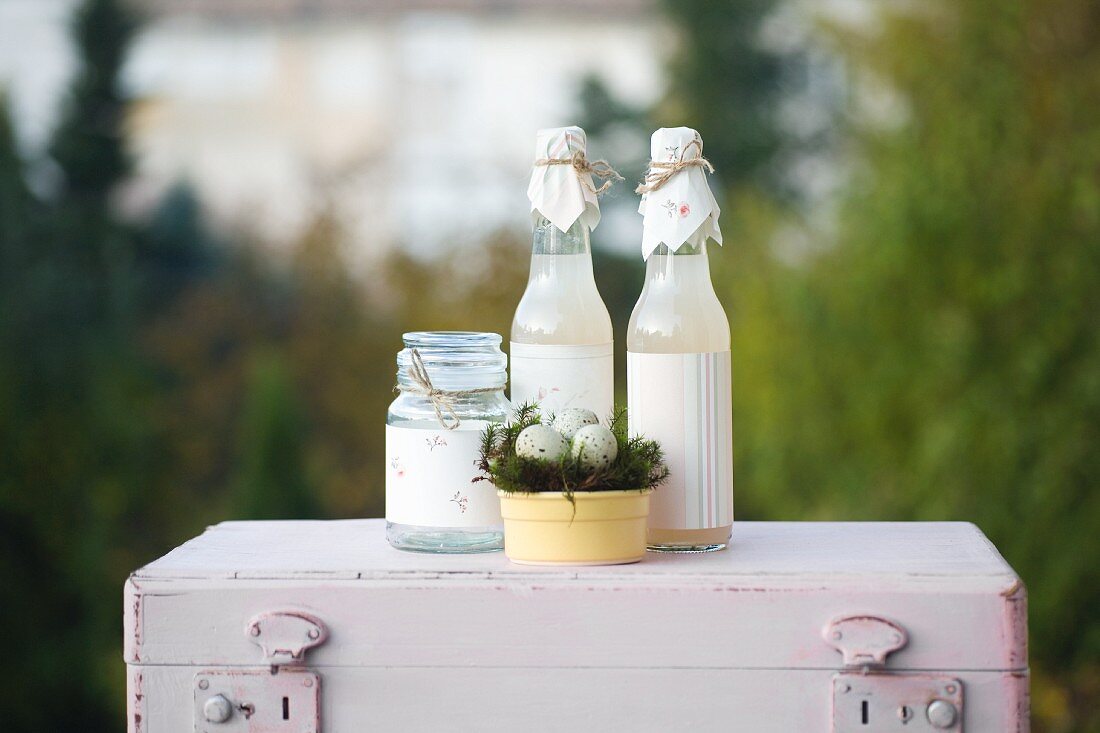 Easter arrangement: jar and bottles decorated with paper and Easter nest of quails' eggs on top of pink vintage suitcase