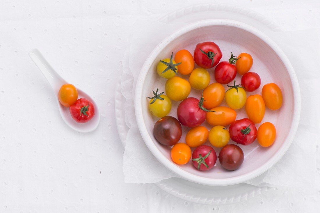 Verschiedenfarbige Tomaten in Porzellanschale & auf Löffel (Aufsicht)