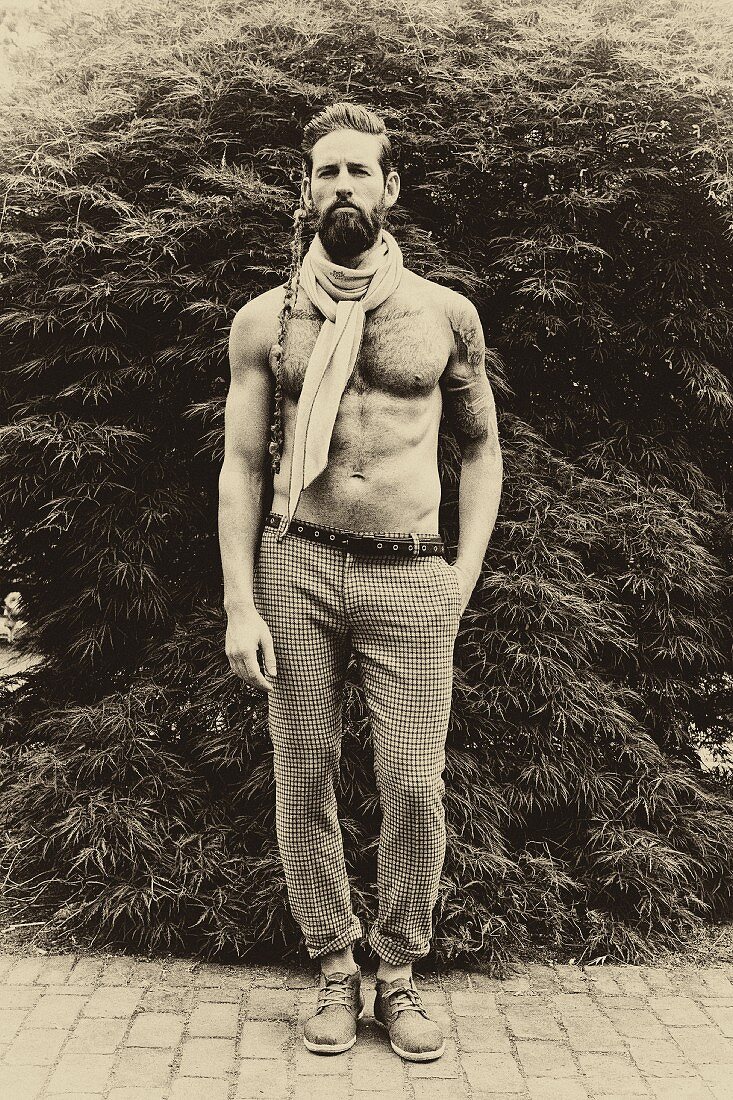 A topless man wearing tweed trousers and a scarf
