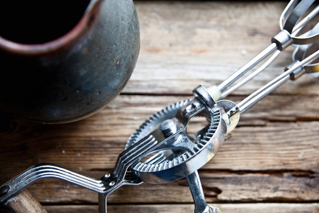 A vintage hand whisk next to a clay jug (detail)