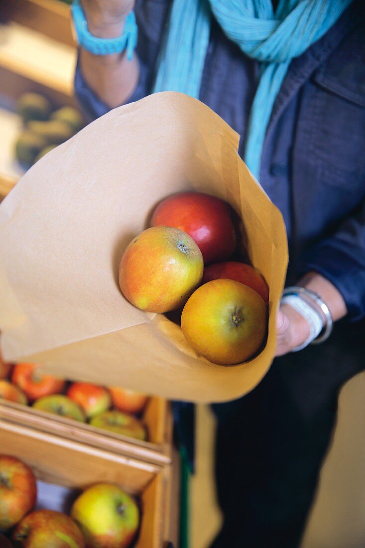 A woman holding a paper bag of organic apples