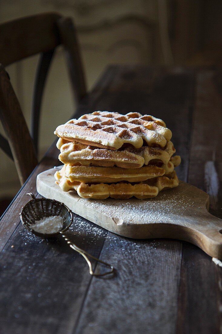 Waffles with icing sugar on a wooden board on a wooden bench