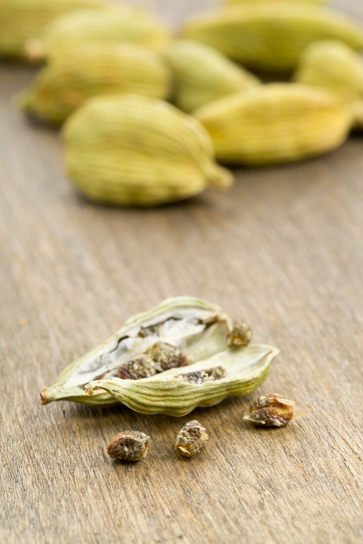 Cardamom seeds on a wooden board with cardamom pods in the background