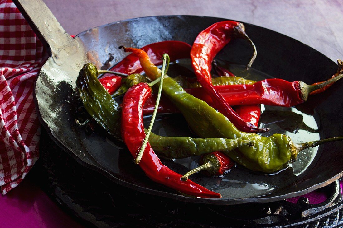 Red and green chillis fried in olive oil in a black cast-iron pan
