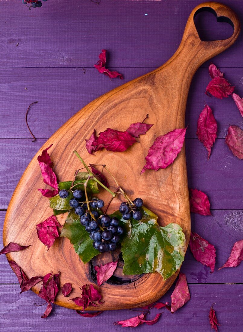 Grapes and autumnal leaves on a wooden board