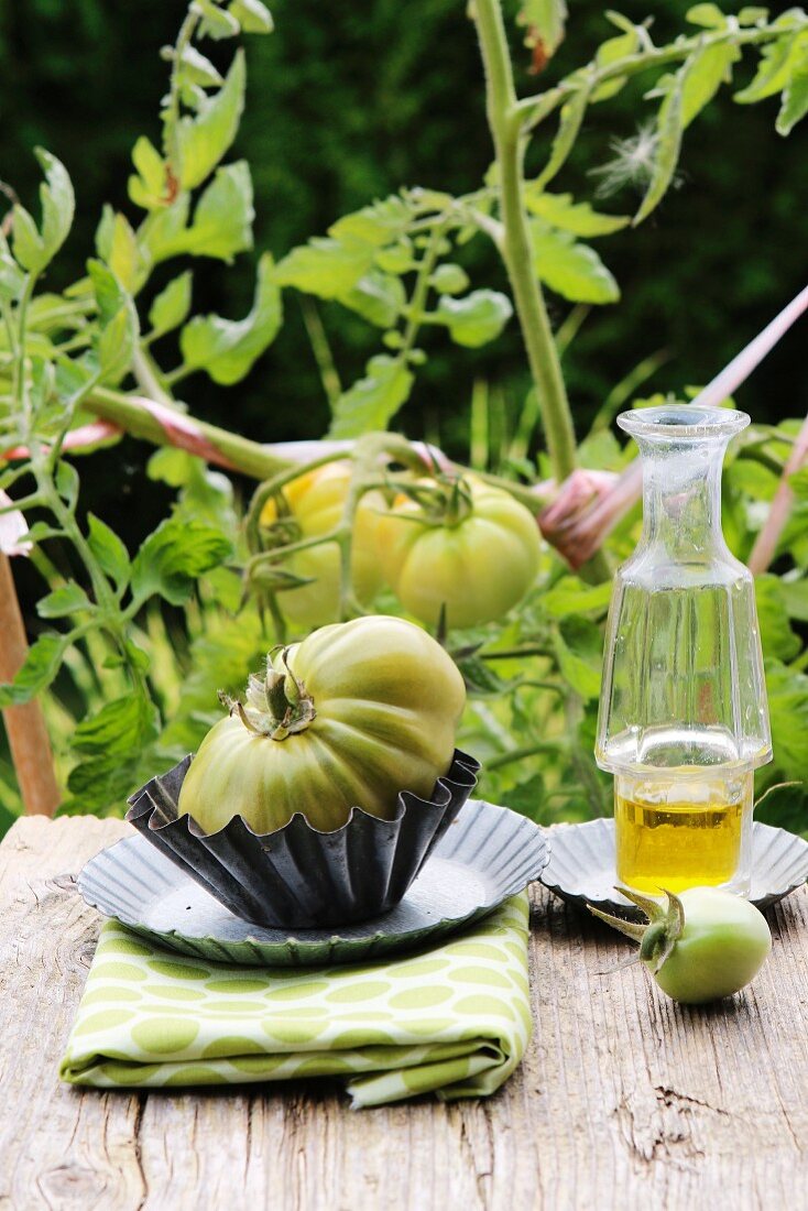 Grüne Tomaten an der Staude und Tomate mit Olivenölflasche auf rustikalem Holzbrett