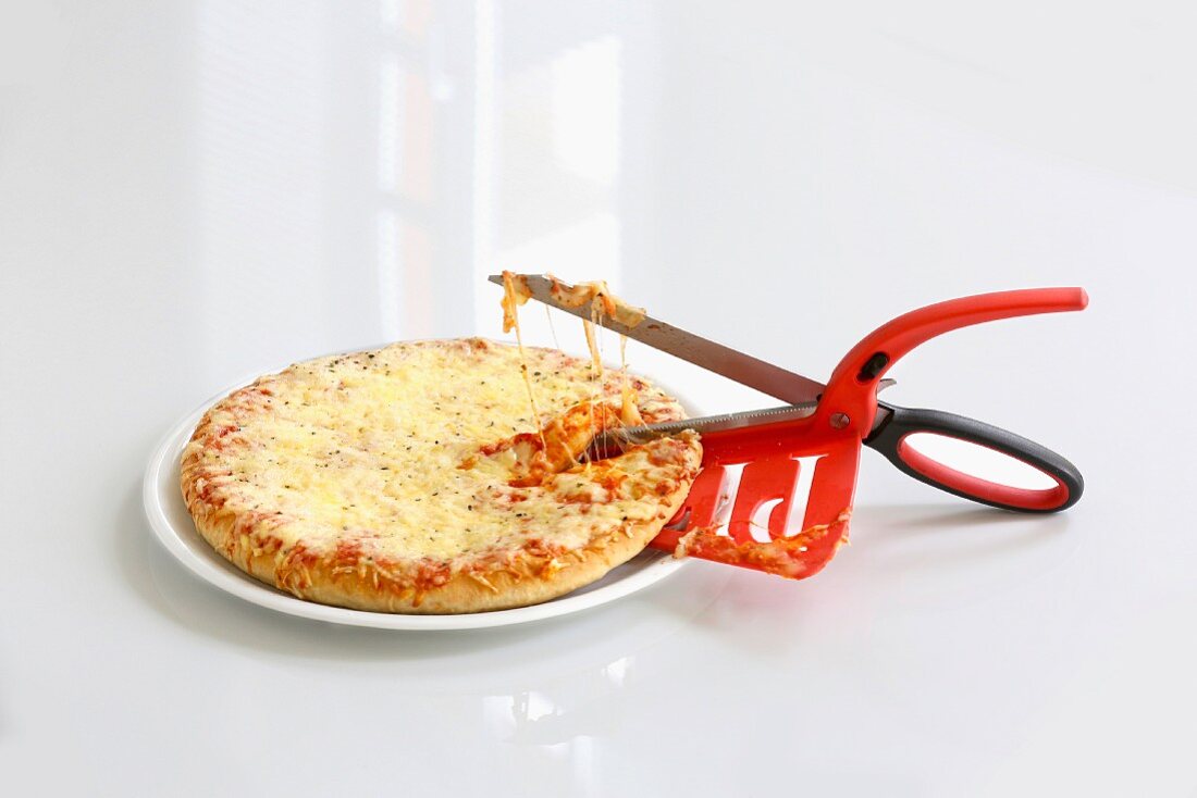 Pizza mit Pizzaschere vor weißem Hintergrund