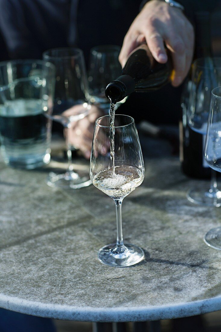 Weinverkostung: Weißwein wird in Glas gegossen