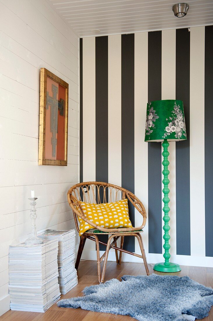 Rattan chair in corner of room against black and white striped wall and next to green retro standard lamp