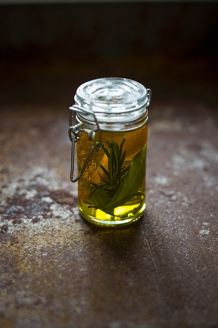 A jar of oil with orange zest and herbs