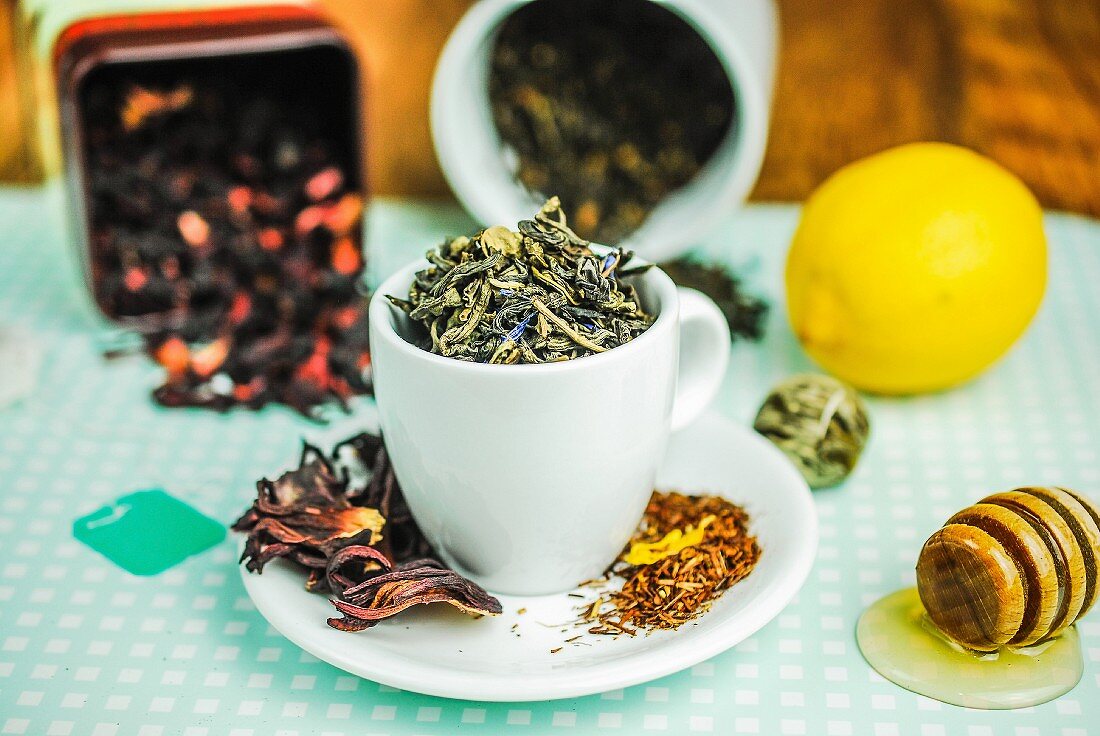 Teeblätter in einer Tasse (Grüntee, Rooibos, Hibiskus), Honig und Zitrone