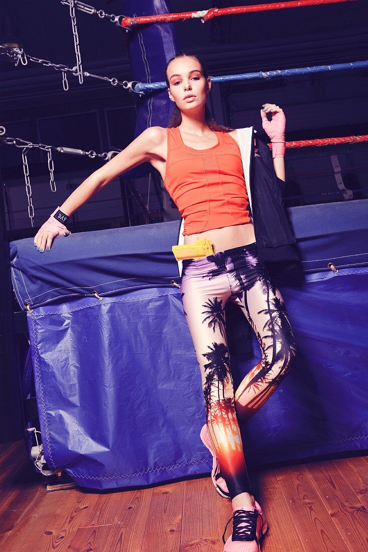 Junge Frau in Trägertop und bedruckter Hose steht an Boxring