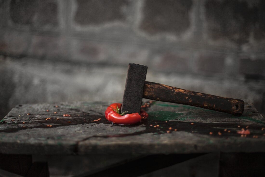 A squashed tomato with a hammer on a wooden table